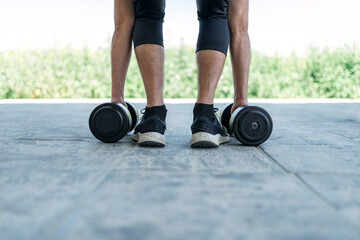 Outdoor training. Male athlete bending down to grasp the alterphilic dumbbells with his hands.