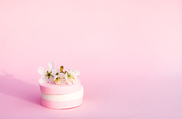 Cosmetic sponges and tree branch with spring flowers on pink background.