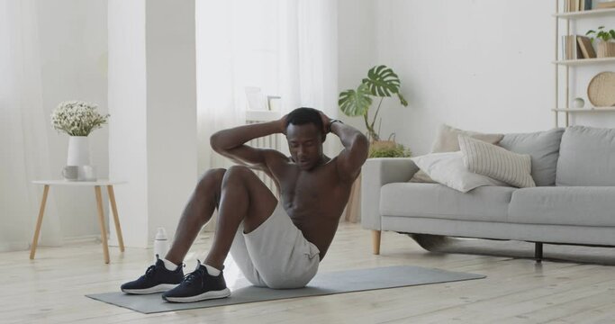 Athletic shirtless african american man doing crisscross crunch exercises, lying on floor at home