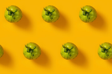 Pattern from raw fresh green striped tomatoes arranged diagonally on yellow background. Minimalist style. Concept of green house life style and products of subsistence farming, flat lay