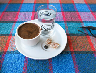 Traditional Turkish Coffee with Turkish delight, water and coffee bean. Glass of water and Turkish delight next to cup. There is a glass on the table over the tablecloth.