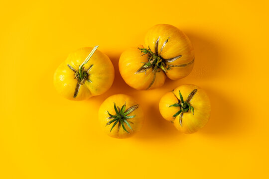 Different raw fresh yellow tomatoes on yellow background. Concept of green house life style and products of subsistence farming, flat lay, copy space