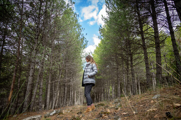 Mujer de pelo largo  con abrigo de plumas dando un paseo por el monte entre árboles
