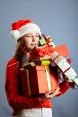 Joyful woman woman holding a lot of boxes with gifts on a gray background.