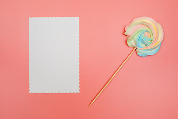 Blank white postcard and rainbow meringue on a stick on a pink background. Christmas, New Year, Valentine's Day, International Women's Day or Mother's Day composition. Flat lay with copy space.