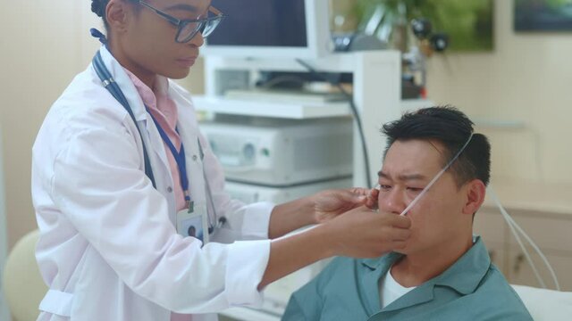 African american black doctor wearing nasal cannula for unhealthy sick asian male patient in hospital room for extra oxygen sup-ply. Medical concept. Surgery. Heaolthcare.
