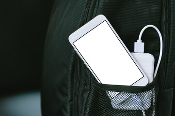 A power bank charges a smartphone in a pocket of a black backpack, on a dark background.