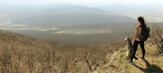 hiking woman with a backpack standing on a mountain cliff with a siberian husky dog enjoying the view © Oszkár Dániel Gáti