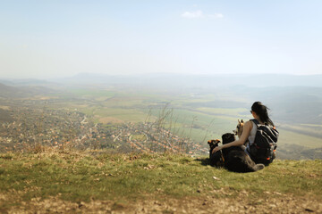 hiking woman with a backpack sitting on a mountain top with three dogs enjoying the view