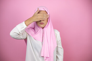 Young beautiful arab woman wearing islamic hijab over isolated pink background serious and covering her eyes with her hand