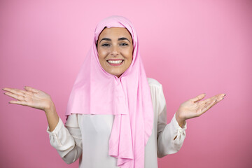 Young beautiful arab woman wearing islamic hijab over isolated pink background clueless and confused expression with arms and hands raised