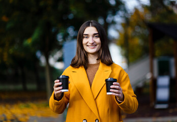 Female hand holding a cup of blank paper on a background of the park. Free space. Hands of a young...