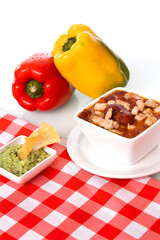 a bowl of soup on a white table with two peppers in the background with checkered tablecloth