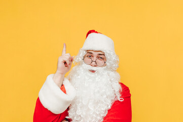 Fototapeta na wymiar Man in a santa costume points his finger up at the copy space and looks at the camera with a serious face. Christmas and New Year concept.