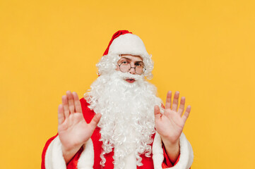 Fototapeta na wymiar Santa Claus shows a stop hand gesture on a yellow background and looks at the camera with a serious face. New year and christmas concept.