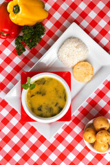 a bowl of soup on a white table with two peppers in the background with checkered tablecloth