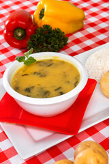 a bowl of soup on a white table with two peppers in the background with checkered tablecloth