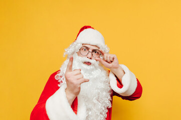 Surprised santa claus isolated on yellow background, looks at camera with shocked face and shows finger. Santa's surprise at Christmas