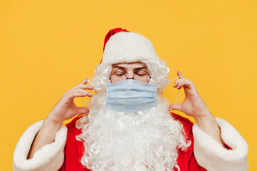 Portrait of funny santa claus wearing protective medical mask on yellow background. Santa is preparing for Christmas in a coronavirus pandemic. - Powered by Adobe