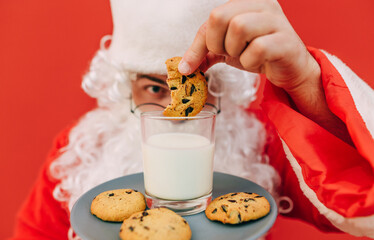 Santa Claus dips Christmas cookies in a glass of milk, close-up cropped photo. Background. Santa eats cookies at Christmas
