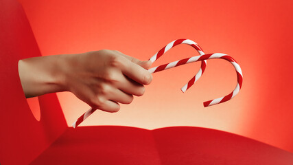 Human hand holding candy cane across paper cut circle on red background. Christmas winter holiday wallpaper.
