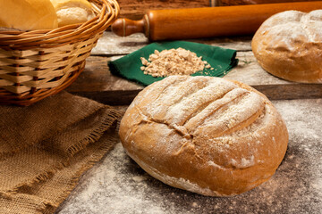 
Homemade round country bread with flour on wooden board with rolling pin, eggs, yeast cloth and rustic cloth with logs in the background