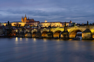 
Charles Bridge on the Vltava river and statues on it and lit street lights and light from lamps at night in the center of Prague in the Czech Republic and there are clouds in the sky