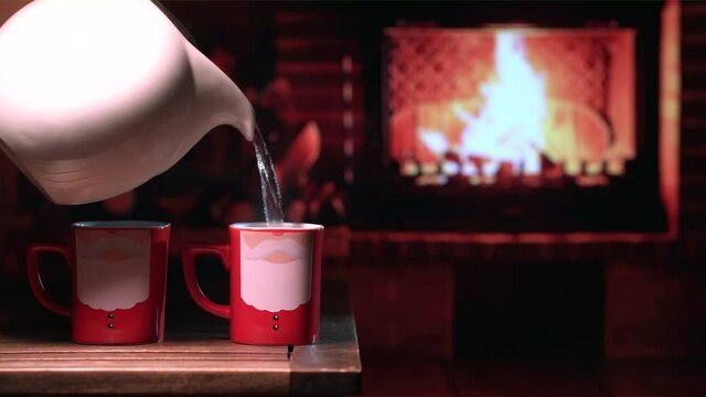 A cup oMugs with the image of Santa Claus in front of the fireplace. Festive cozy Christmas or New Year mood.f hot tea in front of the fireplace on a cozy evening. Festive mood
