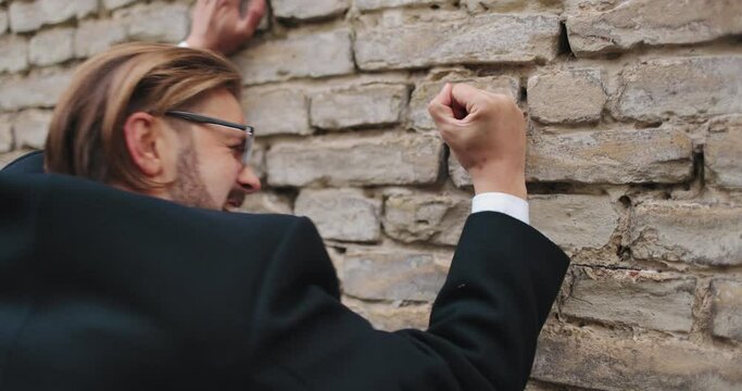 Side view of male entrepreneur in formal wear hitting brick wall with fist and shouting. Mature man relieve stress from work. Concept of feelings.