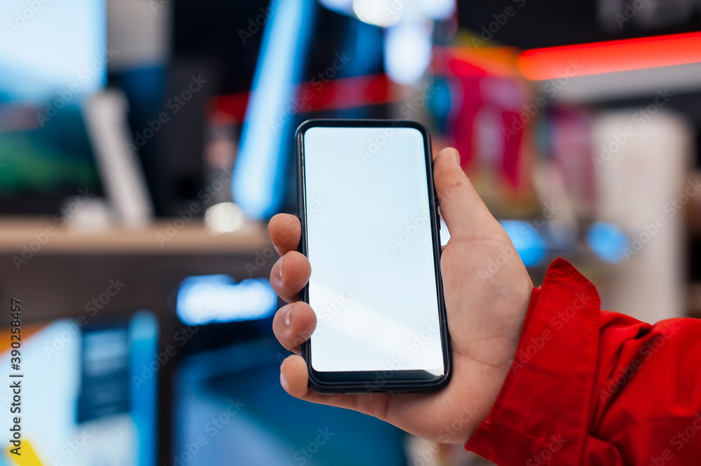Poster mock-up of a smartphone with a white screen in the hands of a man. phone on the background of tvs in