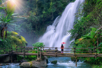  Asian woman tourist  stands on a bamboo bridge watching Pha Dok Siew Waterfall at Doi Inthanon National Park, Chiang Mai Province, Thailand