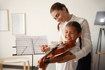 Young woman teaching little girl to play violin indoors © New Africa