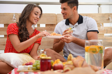 Obraz na płótnie Canvas Happy couple with tasty food and drinks imitating picnic at home
