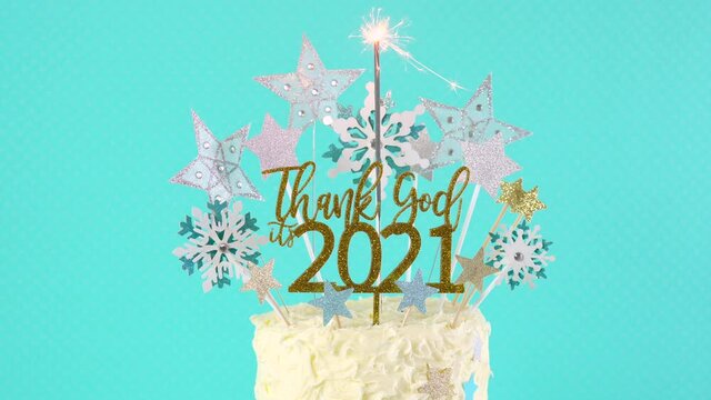 Happy New Year's Eve celebration cake on cake stand in blue white and gold theme decorated with stars and humorous, Thank God It's 2021, cake topper decoration. Closeup with burning sparkler.