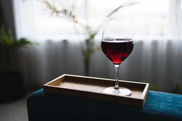 glass of red wine on bamboo tray in living room with window and plants in the background