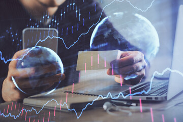 Double exposure of man's hands holding and using a phone and financial graph drawing. Analysis concept.