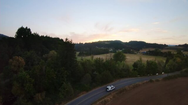Single Van travels down empty highway in farmland during sunset.