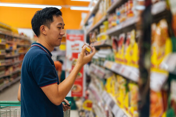 Side view of Asian man shopping in grocery store, buying food, standing in supermarket aisle...