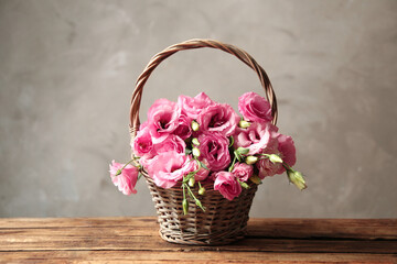 Fototapeta na wymiar Beautiful pink Eustoma flowers in wicker basket on wooden table against grey background