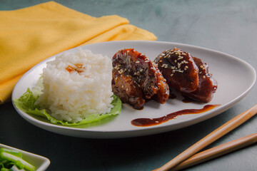 Plate of chicken wings bathed in oyster sauce decorated with sesame seeds and accompanied by white rice.