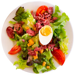 Deliciously french salad of lettuce, sausage, tomatoes and boiled egg. Isolated over white background