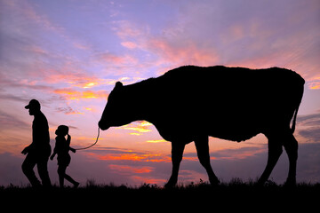 夕陽を背景に草原の牧場で牛を曳く老人と女の子のシルエット
