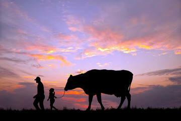 夕陽を背景に草原の牧場で牛を曳く老人と女の子のシルエット