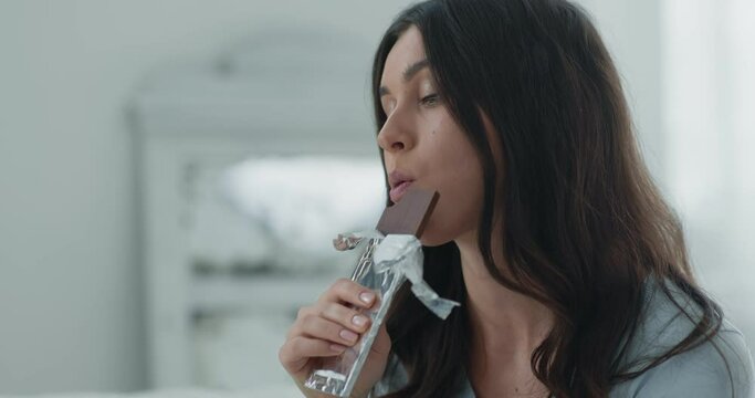 Seizing stress. Close up portrait of young depressed woman eating chocolate bar slow motion