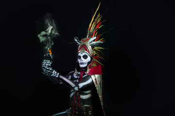 hombre latino , catrin de dios azteca, calavera prehispanica, con saumerio e incienso y fuego, portado penacho de plumas amarillas y rojas en fondo negro, dia de muertos, 1 de noviembre, calaca,