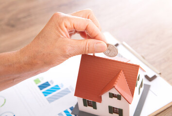 Hand holding a dollar coin ready to cast on the small house model