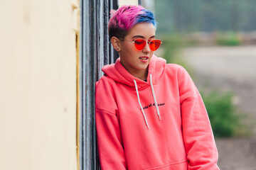 Portrait of a young girl with short colorful hair and nose piercing satanding near the wall with...