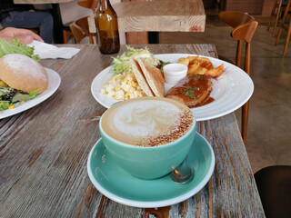 Coffee with Beautiful latte art of cream on top, sandwich, chips/French fries/potato wedge, vegetarian beef at wood table with beer bottle in vintage background at a cafe in Hong Kong