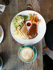 Coffee with Beautiful latte art of cream on top, sandwich, chips/French fries/potato wedge, vegetarian beef at wood table with beer bottle in vintage background at a cafe in Hong Kong