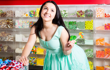 sexy woman posing in the store with lolly on the background of counters with sweets